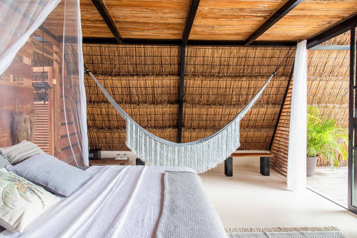Un hamac suspendu à un plafond en bois, un lit avec des oreillers et une structure de toit en chaume.