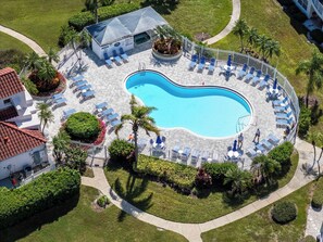 A circular swimming pool with lounge chairs and a covered area, surrounded by well-maintained lawns and palm trees.