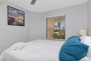 Un dormitorio con cama, ventana con persianas, un cuadro en la pared y un ventilador de techo.