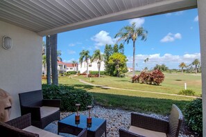 Eine Außenpatio-Terrasse mit Korbmöbeln und Blick auf einen gepflegten Rasen sowie Gebäude in der Ferne.