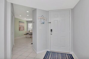 A hallway with a white door, a rug, and a dining area with a table and chairs.