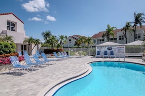 A swimming pool with lounge chairs, a fenced area, and a building with a red roof. - Isla Del Sol 1st Floor 2BD/2BA. Close to Beaches (St. Petersburg)