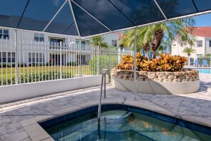 Zona de piscina con cerca blanca, una jardinera de piedra con plantas y vista despejada a un edificio al fondo.