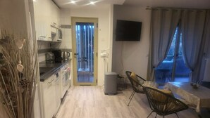 Une cuisine moderne avec des meubles blancs, un coin repas comprenant une table et des chaises, et un téléviseur fixé au mur.