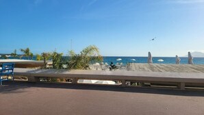 Une vue sur la plage avec une barrière en béton, des palmiers et des parasols de plage.