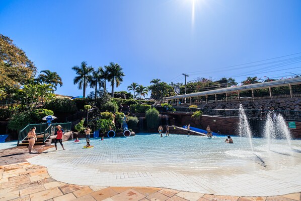 A water park with a swimming pool, palm trees, and a covered walkway.