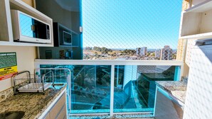 A kitchen with a view of a cityscape through a glass window, a microwave, and a sink with a faucet. - Piazza diRoma - Vacia Temporada (Caldas Novas)