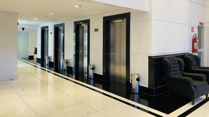 A modern hotel lobby with a long reception desk, black upholstered seating, and a fire extinguisher on the wall. - Piazza diRoma - Vacia Temporada (Caldas Novas)