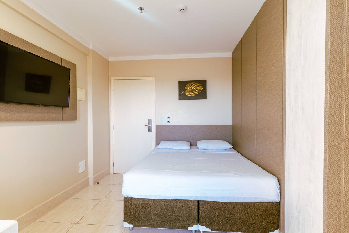 Una habitación de hotel con cama, un televisor de pantalla plana en la pared y una puerta.