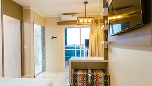 A hotel room with a bed, a small table, a mirror, a window with curtains, and a shower area. - Piazza diRoma - Vacia Temporada (Caldas Novas)