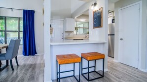 Una cocina moderna con encimera blanca, dos taburetes y una lámpara colgante.