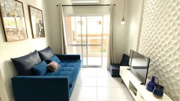 A modern living room with a blue sofa, a flat-screen TV, and a white console table. - Apto novo e arejado com uma ampla sacada (Bertioga)