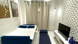 A modern hotel room with a bed, a bench, a TV, and a wall-mounted air conditioner. - Apto novo e arejado com uma ampla sacada (Bertioga)
