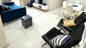 A modern living room with a sofa, a black chair, a TV, and a dining area. - Apto novo e arejado com uma ampla sacada (Bertioga)
