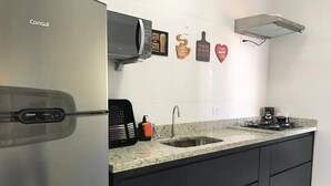 A modern kitchen with a stainless steel refrigerator, a built-in microwave, a granite countertop, a sink, and black cabinets. - Apto novo e arejado com uma ampla sacada (Bertioga)