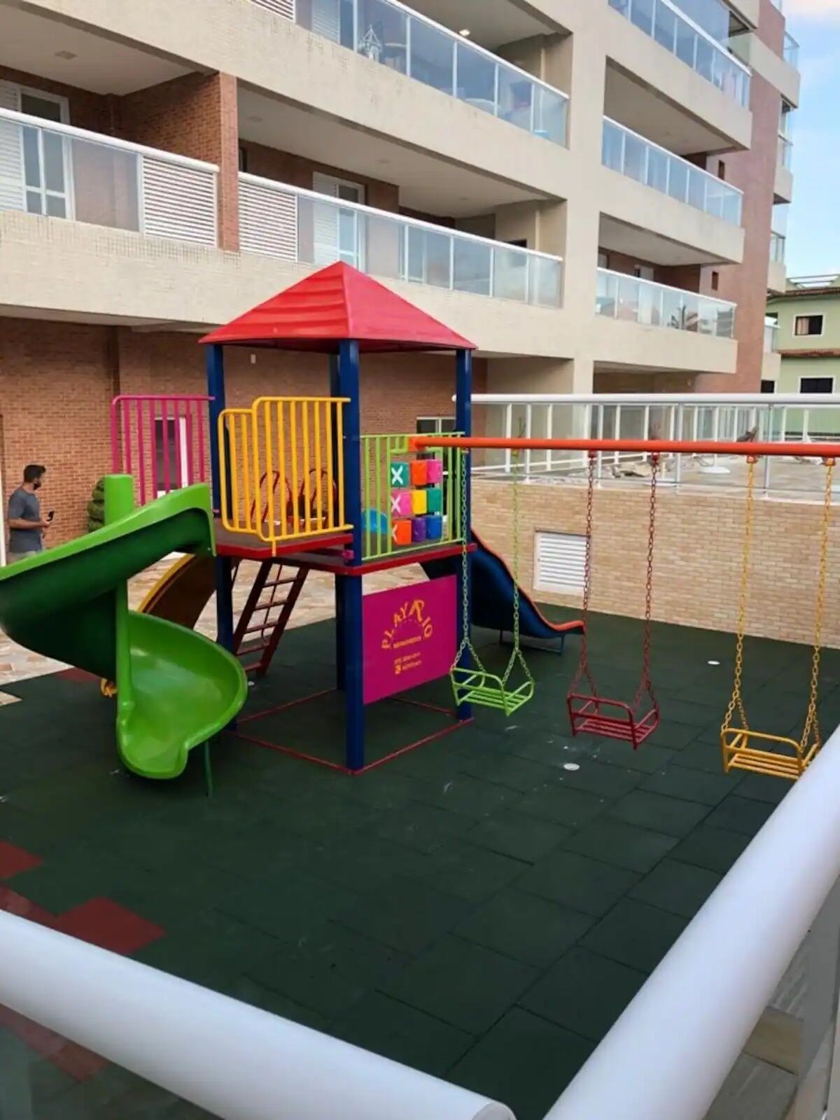Un terrain de jeux avec des toboggans et des balançoires, entouré d’un bâtiment doté de balcons.