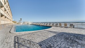 Ein Schwimmbecken mit geschwungener Kante, umgeben von einem gepflasterten Gehweg und einer Geländer.