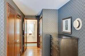 Stylish hallway with a wardrobe, mirror, and framed artwork, leading to a room with a white curtain.