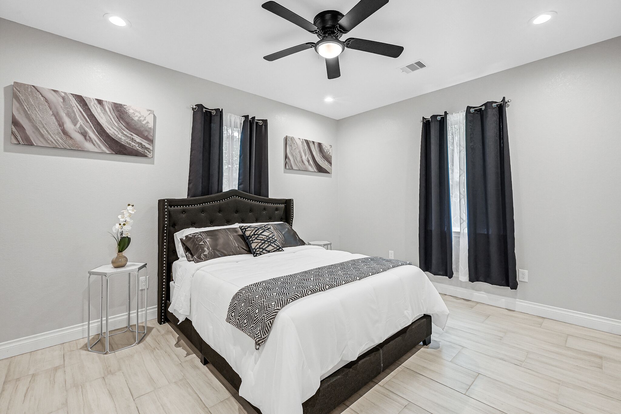 Ein Schlafzimmer mit einem Bett, einem Deckenventilator und Kunstwerken an den Wänden.