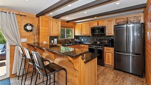 Une cuisine moderne avec des meubles en bois, des appareils en acier inoxydable et un coin bar avec des tabourets.