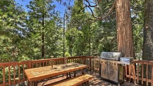 Une terrasse en bois avec une table de pique-nique et un barbecue, entourée d’arbres.