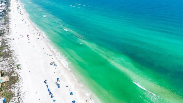 Luchtbeeld van een strand met helder turquoise water, een zandstrand en een rij strandparasols.