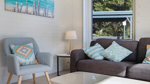 A living room with a grey armchair, a brown sofa, and a small table with a lamp. - Calendo Apartmnts - Unit 1: Ground Floor (Merimbula)