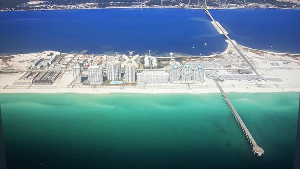 Ein Luftbild eines Küstenresorts mit mehreren Hochhäusern, einer langen Mole, die ins Meer ragt, und einem Sandstrand.