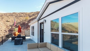 Une terrasse extérieure moderne, dotée d’un espace salon confortable, d’un drapeau et offrant une vue sur un paysage vallonné.