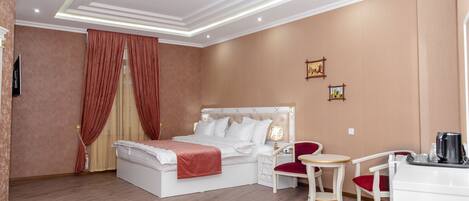 A hotel room with a large bed, a desk with a chair, a small round table, and a coffee machine.
