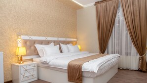 Un dormitorio moderno con cabecera capitonada, ropa de cama blanca, una mesita de noche con lámpara y un ventanal con cortinas.