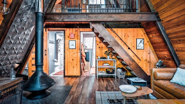 Ein gemütliches Loft mit Holzvertäfelung, einem schwarzen Herd, einer Treppe und einer bequemen Sitzecke.