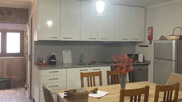 Ett modernt kök med vita skåp, ett matbord med stolar, en hängande lampa och ett kylskåp.