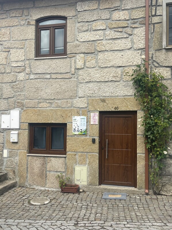 Un bâtiment en pierre avec une porte en bois, une fenêtre et une petite plante en pot.