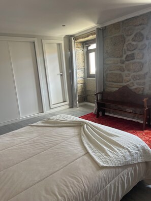 Une chambre avec un lit, un banc en bois, un mur en pierre et une fenêtre.