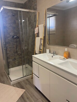 Une salle de bain avec une douche à parois de verre, un lavabo blanc doté d’un distributeur de savon et un miroir.
