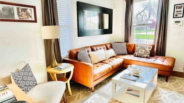 Un salon avec un canapé en cuir marron, une table basse blanche et un tapis à motifs.