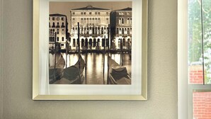 Une photographie encadrée représentant un bâtiment historique avec un canal, un lit recouvert d’une literie blanche et un coussin décoratif à texture.