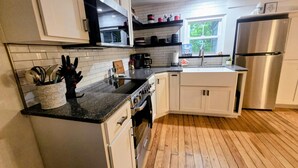 Une cuisine moderne avec des meubles blancs, un réfrigérateur en acier inoxydable, un plancher en bois et une fenêtre donnant sur un paysage verdoyant.
