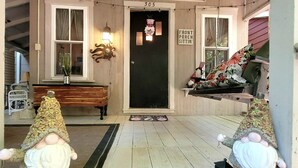 Un porche avec un banc en bois, une statue de gnome décorative, une porte portant le numéro « 305 », et une pancarte indiquant : « On se pose sur le porche ».