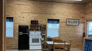 A compact kitchen with wooden walls, a refrigerator, stove, microwave, and a dining table with chairs.