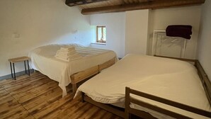 Una habitación con dos camas de madera, un pequeño banco y una ventana.