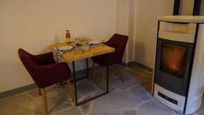 Un comedor con una mesa y dos sillas, una mesita con una botella y vasos, y un estufa de leña.