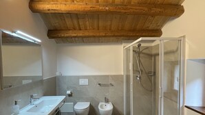 Un baño moderno con techo de madera, una bañera independiente, ducha con mampara de vidrio y tocador con espejo.