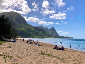 A beach with people sunbathing and swimming, surrounded by mountains and clear skies.