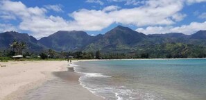Ein Strand mit klarem türkisblauem Wasser, einem Sandufer und einem Bergmassiv im Hintergrund.