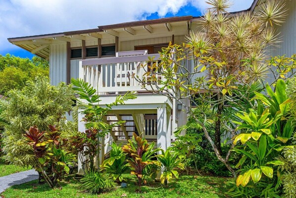 A two-story building with a balcony, surrounded by lush tropical vegetation.