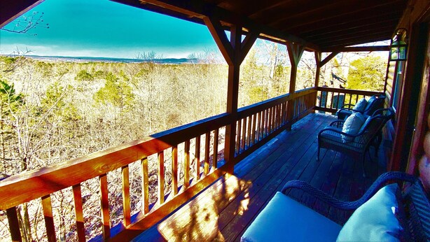 A covered outdoor deck with wooden railings and seating. - Romantic Cabin with Jacuzzi Tub. Ride-in Access to Wolf Pen Gap ATV trails  (Mena)