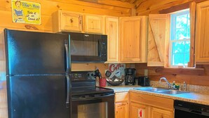 A kitchen with wooden cabinets, a black refrigerator, a stove, and a coffee maker. - Romantic Cabin with Jacuzzi Tub. Ride-in Access to Wolf Pen Gap ATV trails  (Mena)