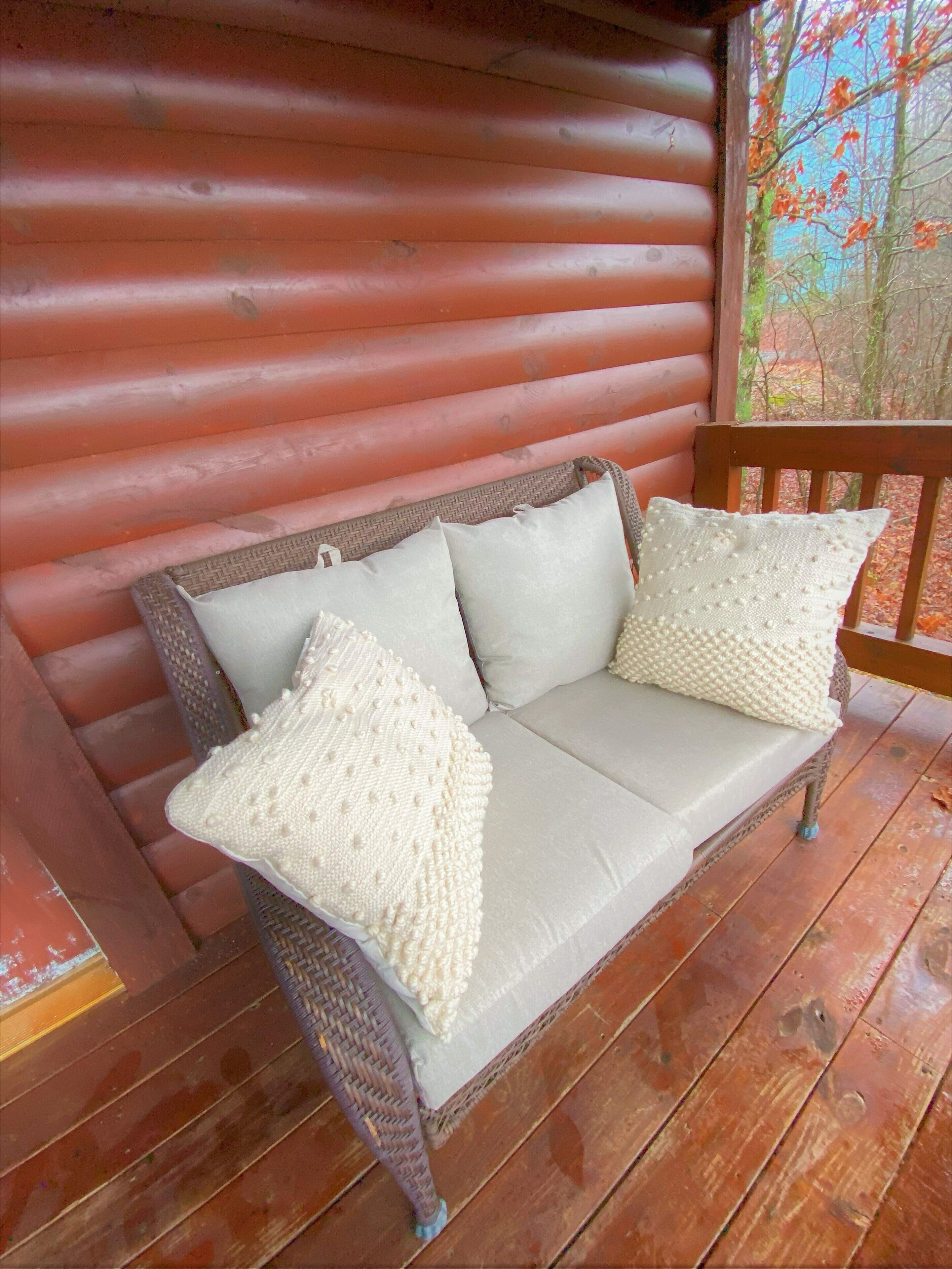 A wicker sofa with two pillows on a wooden deck.